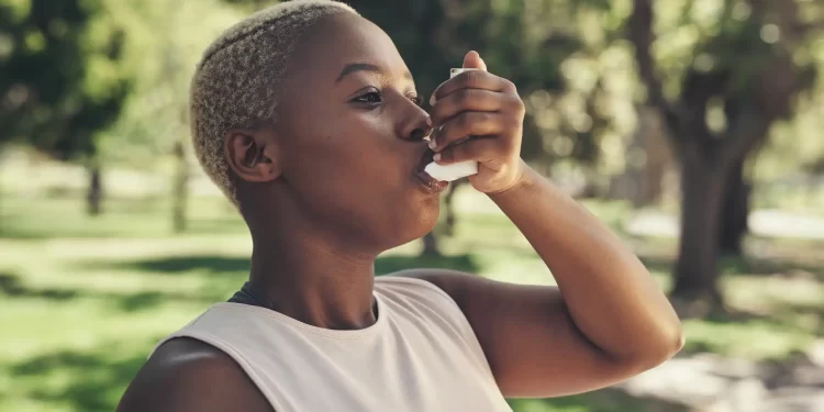 Black woman uses asthma inhaler after exercising outside.